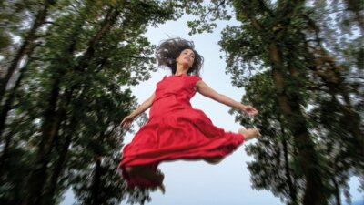 Margherita Vicario in volo con un vestito rosso tra gli alberi, nella foto promozionale dell'album Un tripudio di pelle e di baci