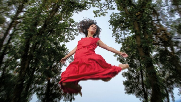 Margherita Vicario in volo con un vestito rosso tra gli alberi, nella foto promozionale dell'album Un tripudio di pelle e di baci