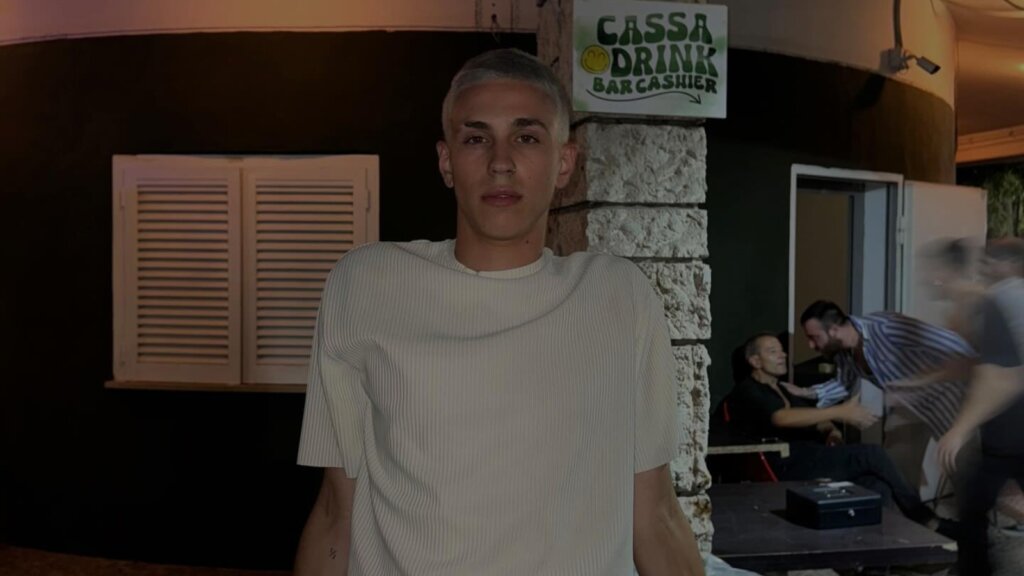 Nicolò Bassani, il cantante entrato ad Amici 26, con una maglia chiara davanti al bancone di un locale