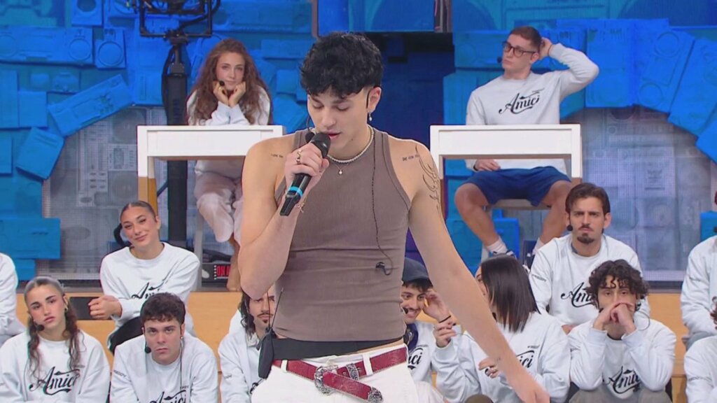 Nicolò Bassani canta Un altro ancora nella prima puntata di Amici 26, con canotta marrone e microfono