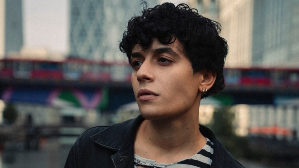 SENZA CRI in primo piano all'aperto, con giacca scura e maglia a righe, nella foto del nuovo EP NO CAP