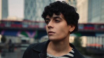 SENZA CRI in primo piano all'aperto, con giacca scura e maglia a righe, nella foto del nuovo EP NO CAP