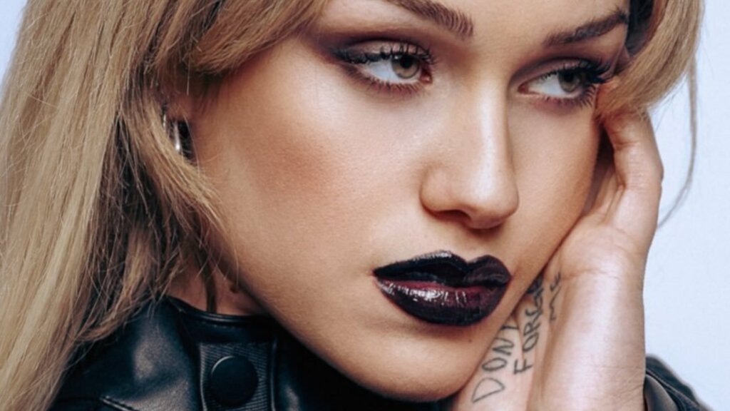 Shari, la cantautrice di Egoista entrata ad Amici 26, in primo piano con il rossetto scuro e la mano sul viso
